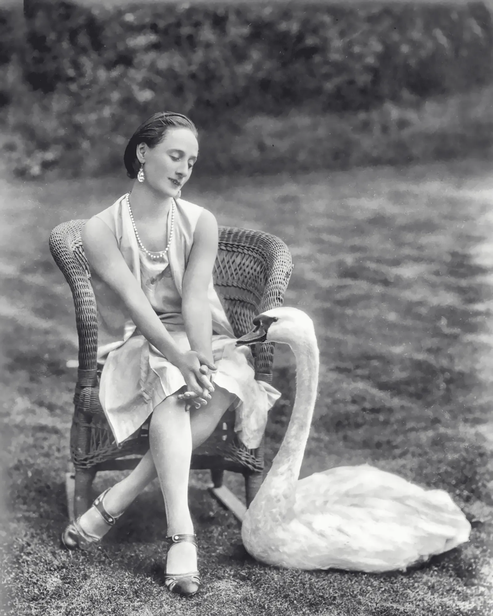 Anna Pavlova zit op een rieten stoel in de tuin en kijkt naar haar witte zwaan